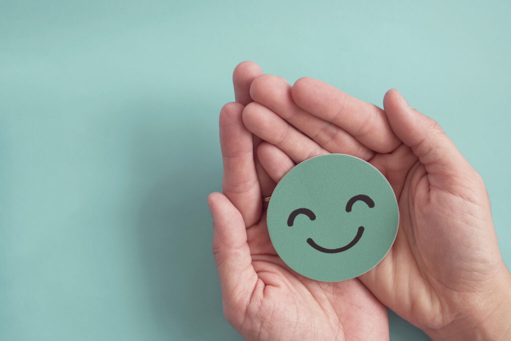 Hands holding green happy smile face paper cut