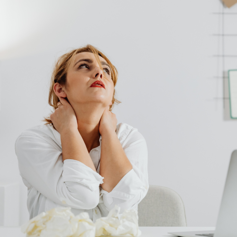 Office worker holding her neck showing signs of work-related stress at her desk